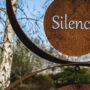 Palabra silencio en inglés escrita en escultura de metal en un bosque