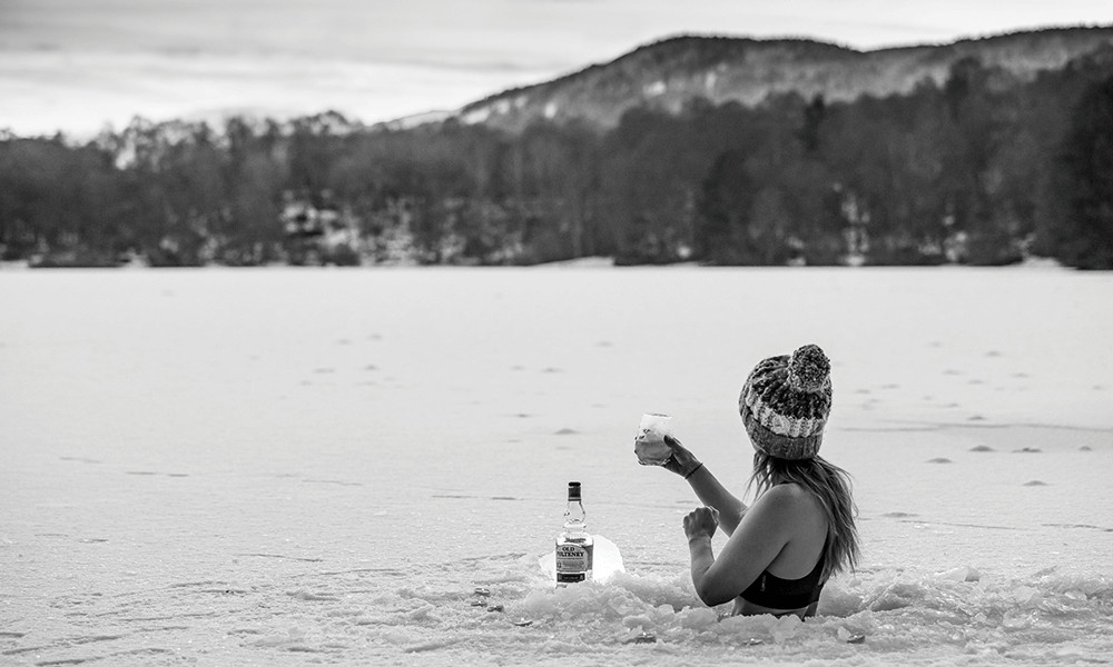 Woman experiencing ice bath benefits on an icy lake, with the upper half of her body above the ice and the lower half in contact with ice-cold water